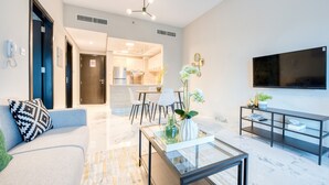 A modern living room with a sofa, coffee table, TV, and a dining area with chairs and a table. - Exceptional 1BR in MAG 5, Emaar South by Deluxe Holiday Homes (Dubai)