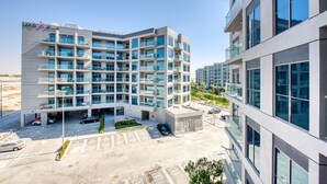 A multi-story hotel with a modern design, featuring balconies on each floor, a parking area, and a clear view of the surrounding area. - Exceptional 1BR in MAG 5, Emaar South by Deluxe Holiday Homes (Dubai)