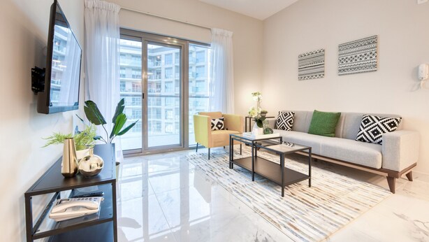 A modern living room with a sofa, coffee table, and a TV mounted on the wall. - Exceptional 1BR in MAG 5, Emaar South by Deluxe Holiday Homes (Dubai)