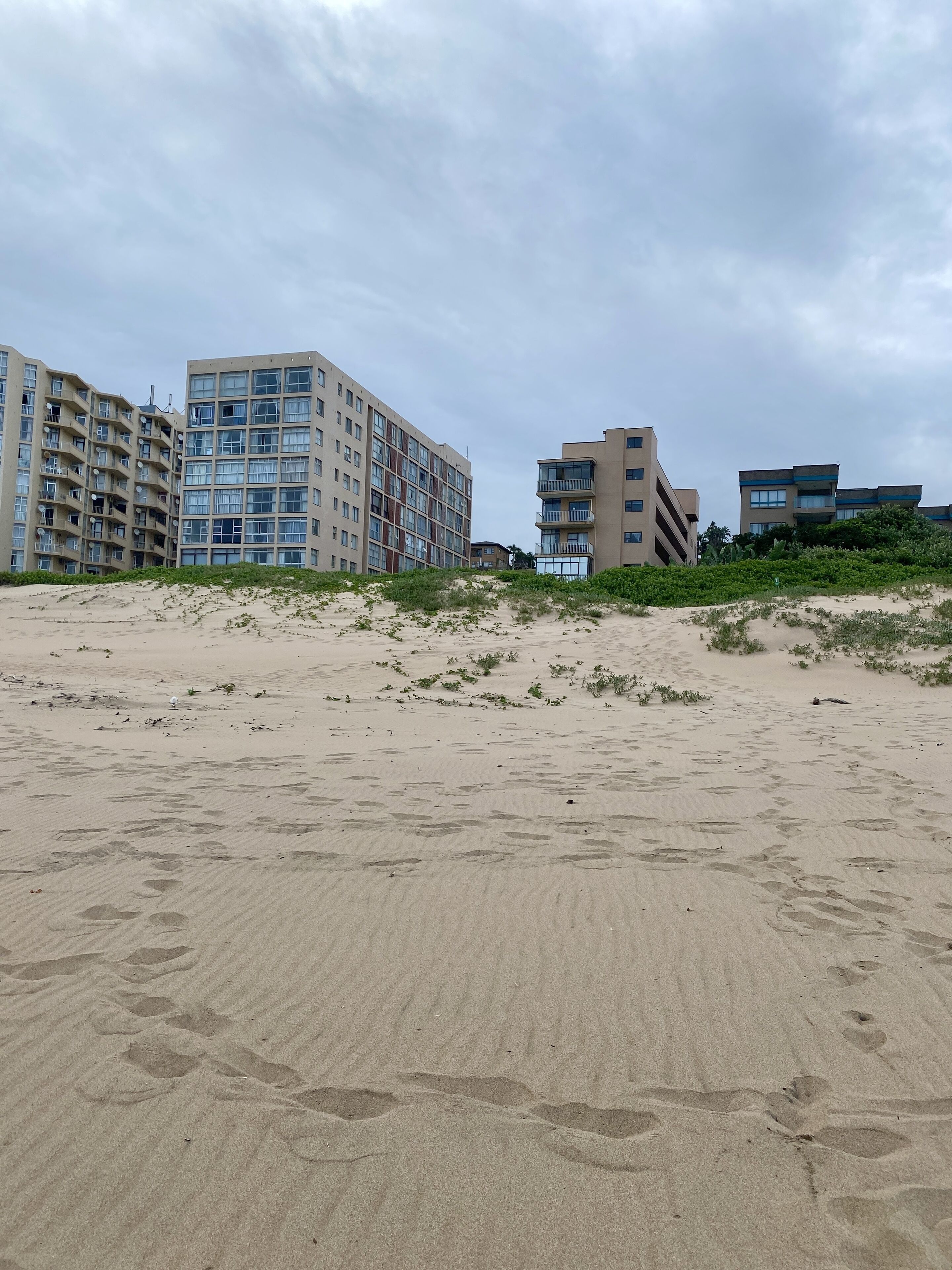 Een zandstrand met voetafdrukken en gebouwen op de achtergrond.