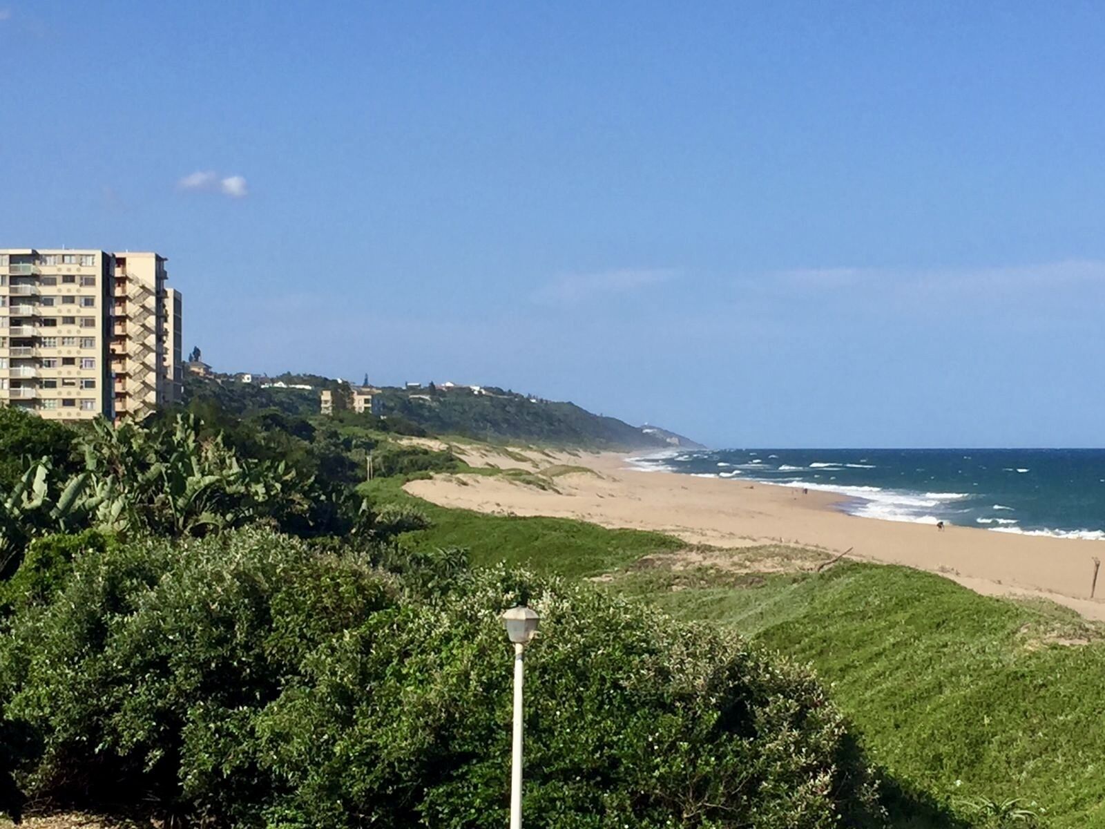 Un paysage côtier avec une plage de sable, un ciel bleu dégagé et un bâtiment doté de nombreux balcons.
