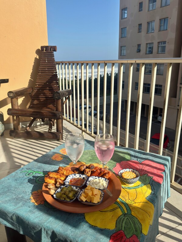 A table with a floral tablecloth, a plate of food, and two glasses of water on a balcony. - Family-friendly, sea and breaker view, 2 min from beach (Amanzimtoti)
