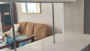 Une cuisine dotée d’un plan de travail en marbre blanc, d’un four encastré et d’un coin repas avec un canapé marron et une table en verre.