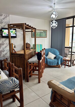 A cozy living room with a wooden coffee table, a blue armchair, and a TV mounted on the wall. - Family-friendly, sea and breaker view, 2 min from beach (Amanzimtoti)