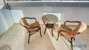 Un balcon avec des fauteuils en osier et une table en verre, offrant une vue sur le paysage urbain.