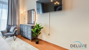 Une pièce moderne avec un canapé gris, une commode bleu foncé, une plante en pot et un téléviseur fixé au mur, agrémenté de jeux de lumière.