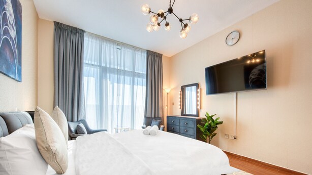 Une chambre d’hôtel avec un grand lit, un téléviseur à écran plat fixé au mur, une table de chevet avec une lampe et une grande fenêtre avec des rideaux.
