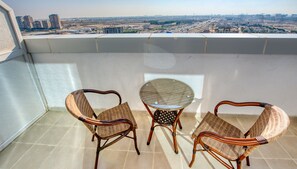 A balcony with wicker chairs and a glass table, overlooking a cityscape. - Elegant Studio in Al Jawhara Tower JVT by Deluxe Holiday Homes (Dubai)