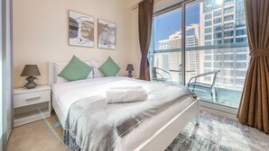 Ein Hotelzimmer mit einem großen Bett, zwei Nachttischen, einem Fenster mit Blick auf Gebäude und einem Balkenstuhl.