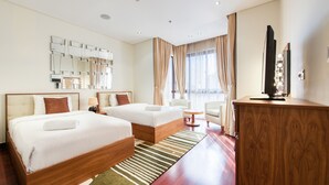 A hotel room with two beds, a desk, a TV, and a large window with curtains.