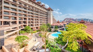 A multi-story hotel with balconies, a swimming pool, and a landscaped area with palm trees.