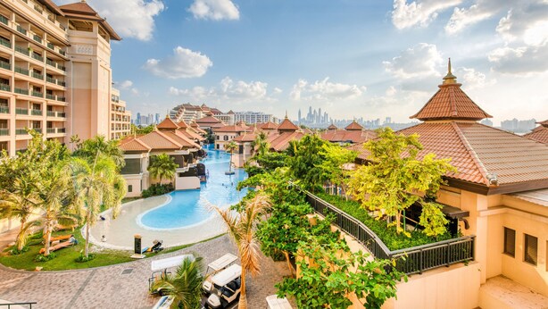 A resort with a swimming pool, palm trees, and a view of the city skyline.