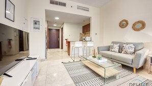 A modern living room with a sofa, coffee table, and TV. There is a kitchen area in the background. - Prime Commercial Hub Near Burj Khalifa Studio Unit, Safeer Tower 1 (Dubai)