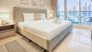 A hotel room with a large bed, a nightstand, a lamp, a view of the city through large windows, and a balcony with chairs. - Prime Commercial Hub Near Burj Khalifa Studio Unit, Safeer Tower 1 (Dubai)
