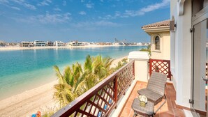 A balcony with a view of a beach and ocean, a wicker chair, and a small table with a vase. - Immaculate 4BR Villa with Assistant Room and Private Pool at Frond O Palm Jumeirah by Deluxe Holiday Homes (Dubai)