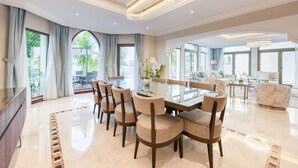 A spacious dining area with a glass table and chairs, large windows with curtains, and a chandelier. - Immaculate 4BR Villa with Assistant Room and Private Pool at Frond O Palm Jumeirah by Deluxe Holiday Homes (Dubai)