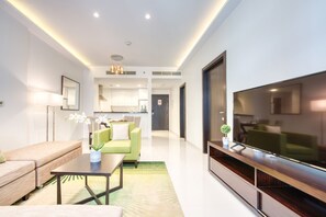 A modern living room with a sofa, coffee table, and TV. There is a kitchen in the background.