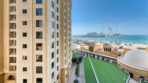 Un hotel moderno de gran altura con varios balcones, un patio central con césped artificial y vistas a la costa, donde se distingue una noria.