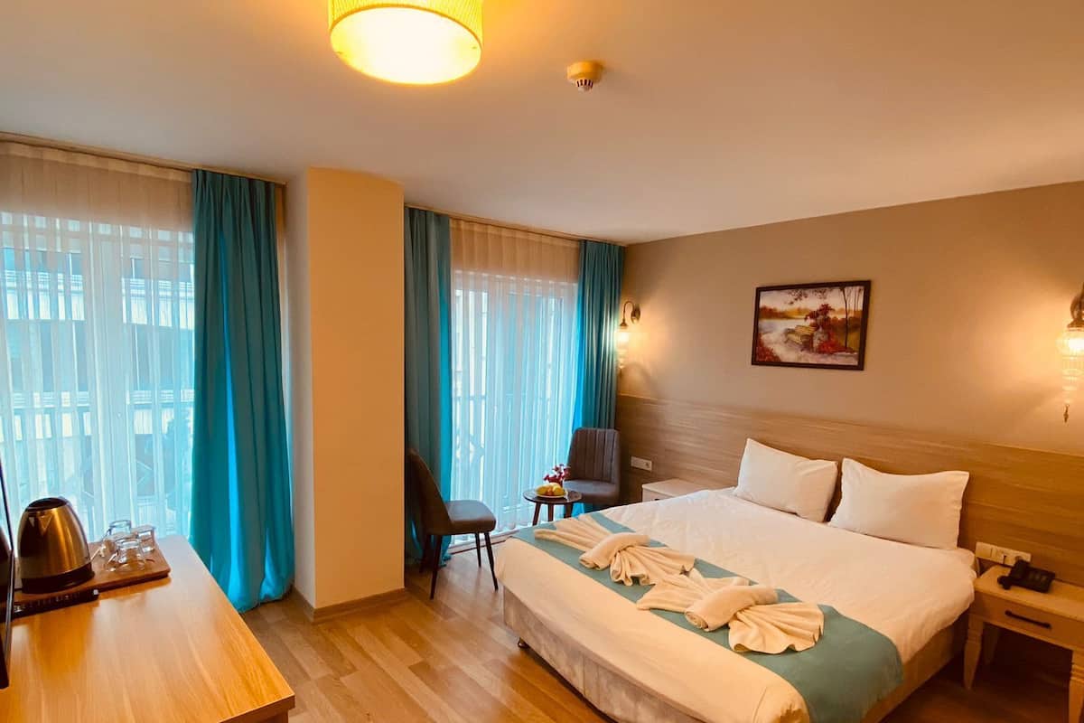 Ein Hotelzimmer mit einem großen Bett, einem Schreibtisch mit Wasserkocher, einem Stuhl und einem kleinen Tisch mit Obstschale.