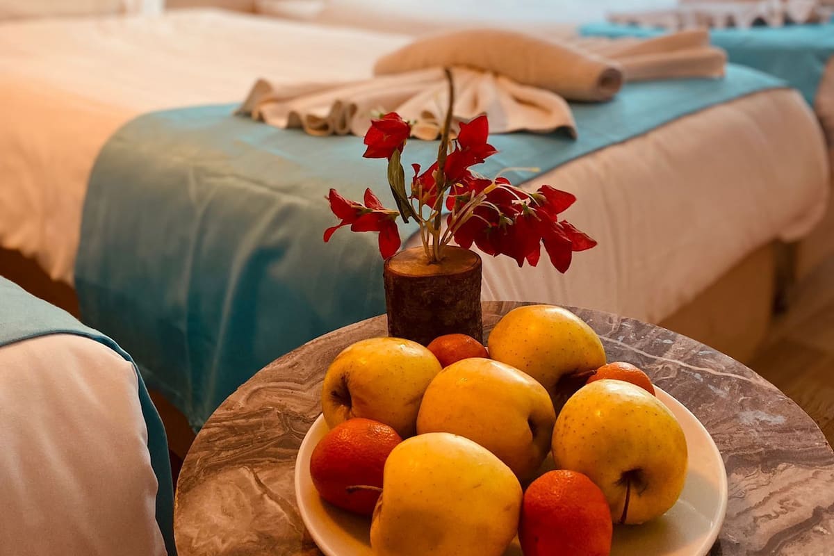 Ein Hotelzimmer mit einem Bett, einem Nachttisch mit Obstplatte und einer Vase mit Blumen.