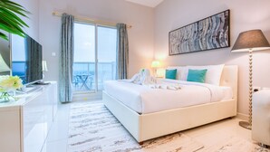 Hotelkamer met een groot bed, een bureau met lamp, een schilderij aan de muur en uitzicht op zee door het raam.