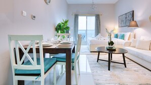 Een moderne woonkamer met een eethoek, witte meubels, een kroonluchter en uitzicht door een groot raam.