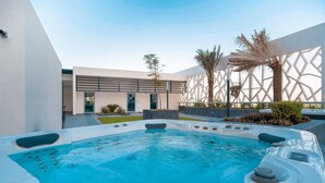 A modern outdoor swimming pool with hot tubs, surrounded by a geometric wall and palm trees.