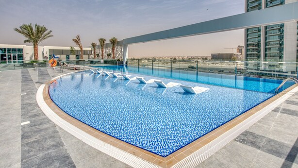 A rooftop pool with clear blue water, surrounded by palm trees and modern buildings.