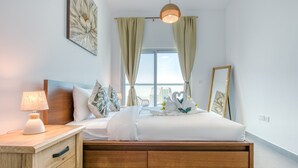 A neatly arranged bedroom with a bed, bedside table, lamp, and a view of the city through large windows.