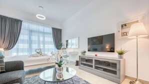 Uma sala de estar moderna com sofá, uma mesa de centro de vidro, televisão e um console com plantas.