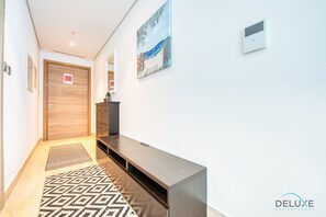Un couloir avec une porte en bois, un banc, un tableau accroché au mur et un thermostat.