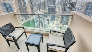 A balcony with wicker furniture, a glass table, and a view of a cityscape with high-rise buildings and a body of water.