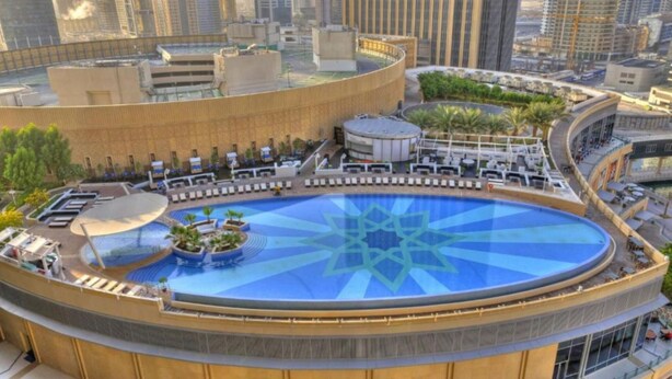 A rooftop pool with a geometric design, surrounded by lounge areas and a cityscape view.