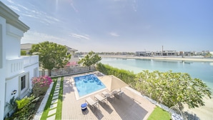 A pool area with a view of the sea, a white building, and a well-maintained garden. - Signature 6BR Villa with Assistant Room and Private Pool in Frond F Palm Jumeirah by Deluxe Holiday Homes (Dubai)