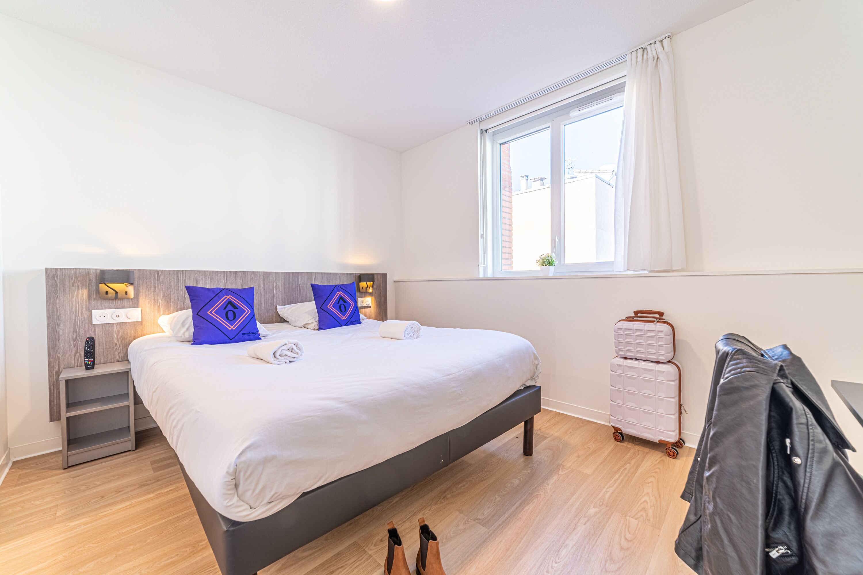 Een moderne hotelkamer met een groot bed, een nachtkastje, een koffer en een kapstok.