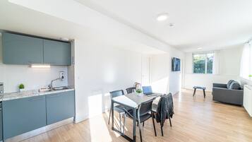 Una cocina moderna con armarios grises, una mesa de comedor con sillas y un sofá gris en un espacio luminoso con piso de madera.
