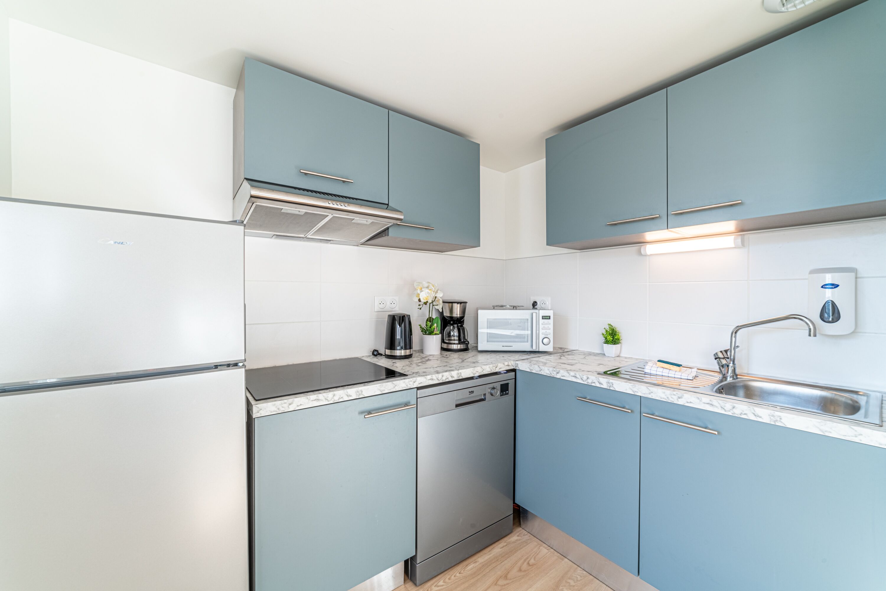 A modern kitchen with light blue cabinets, a stainless steel dishwasher, a built-in oven, a coffee maker, and a microwave.