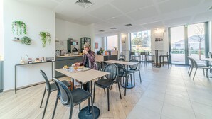 Een modern café met een strak, minimalistisch interieur, inclusief een balie met koffieapparaat, een zitgedeelte met tafels en stoelen, en decoratieve planten aan de muren.