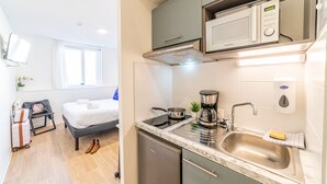 Een kleine keuken met een magnetron, kookplaat, spoelbak en een klein aanrecht.