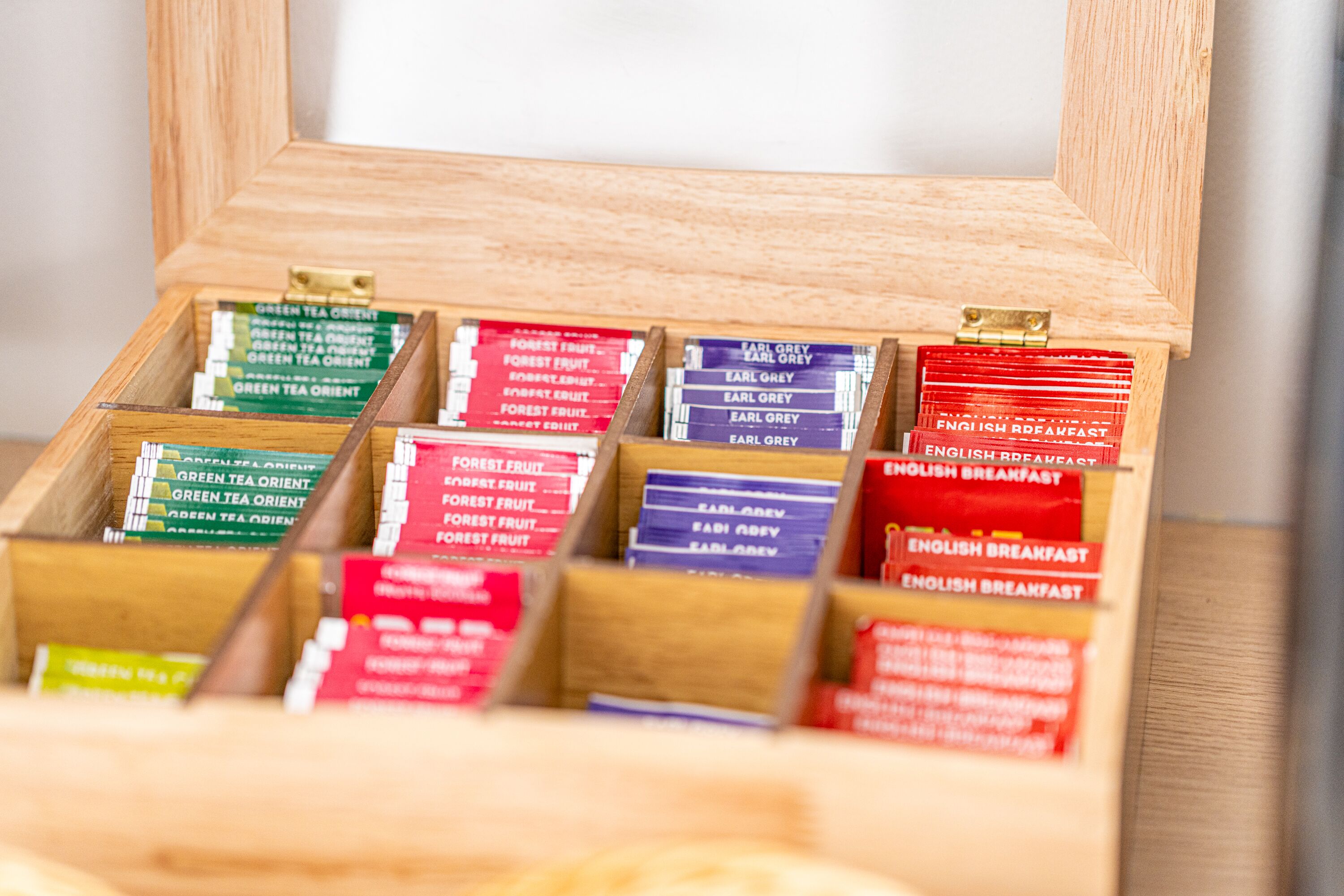 Una caja de madera con compartimentos que contienen bolsitas de té etiquetadas como 'Green Tea Orient' y 'English Breakfast'.