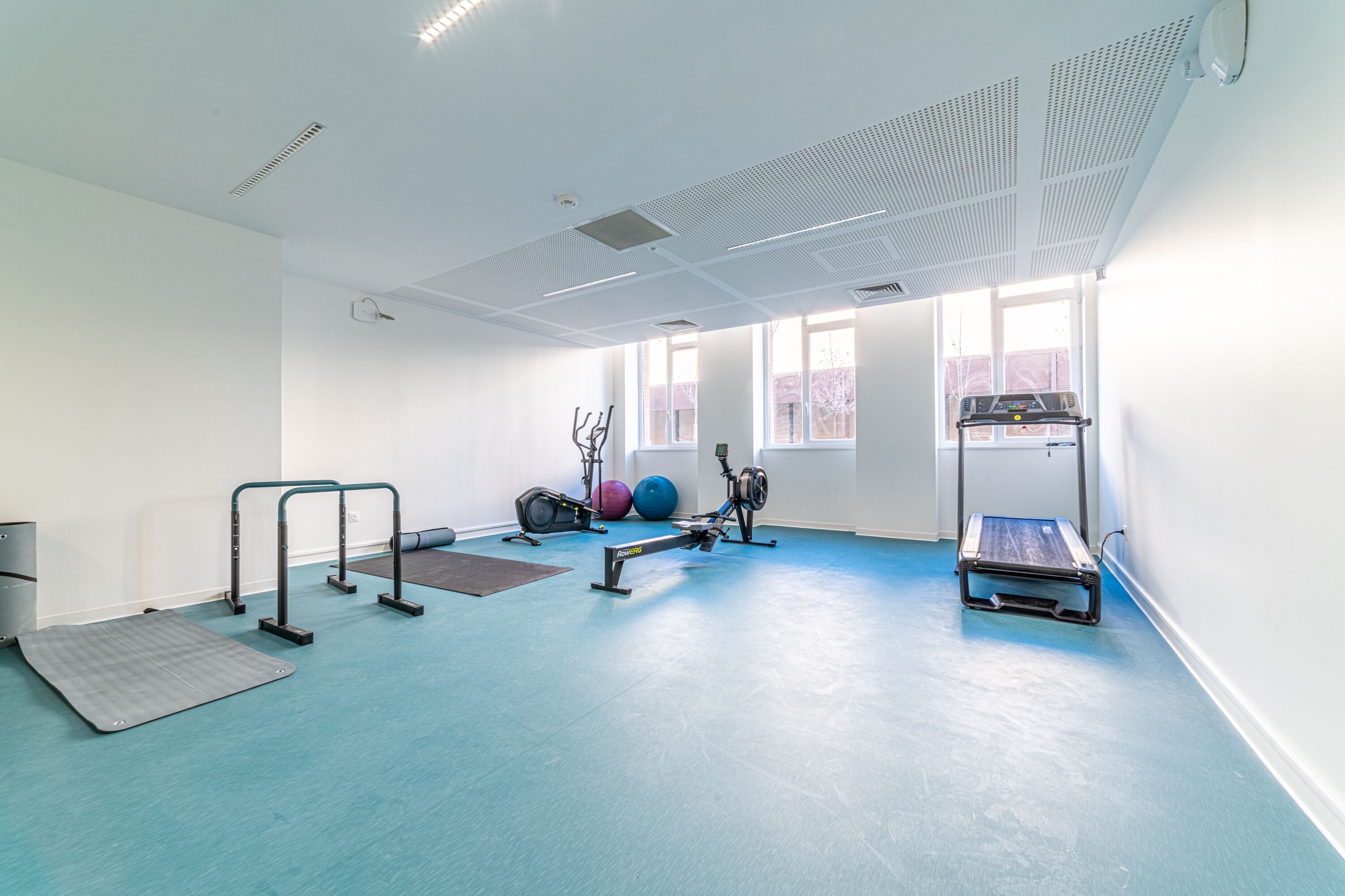 A gym with exercise equipment, a blue floor, and large windows.