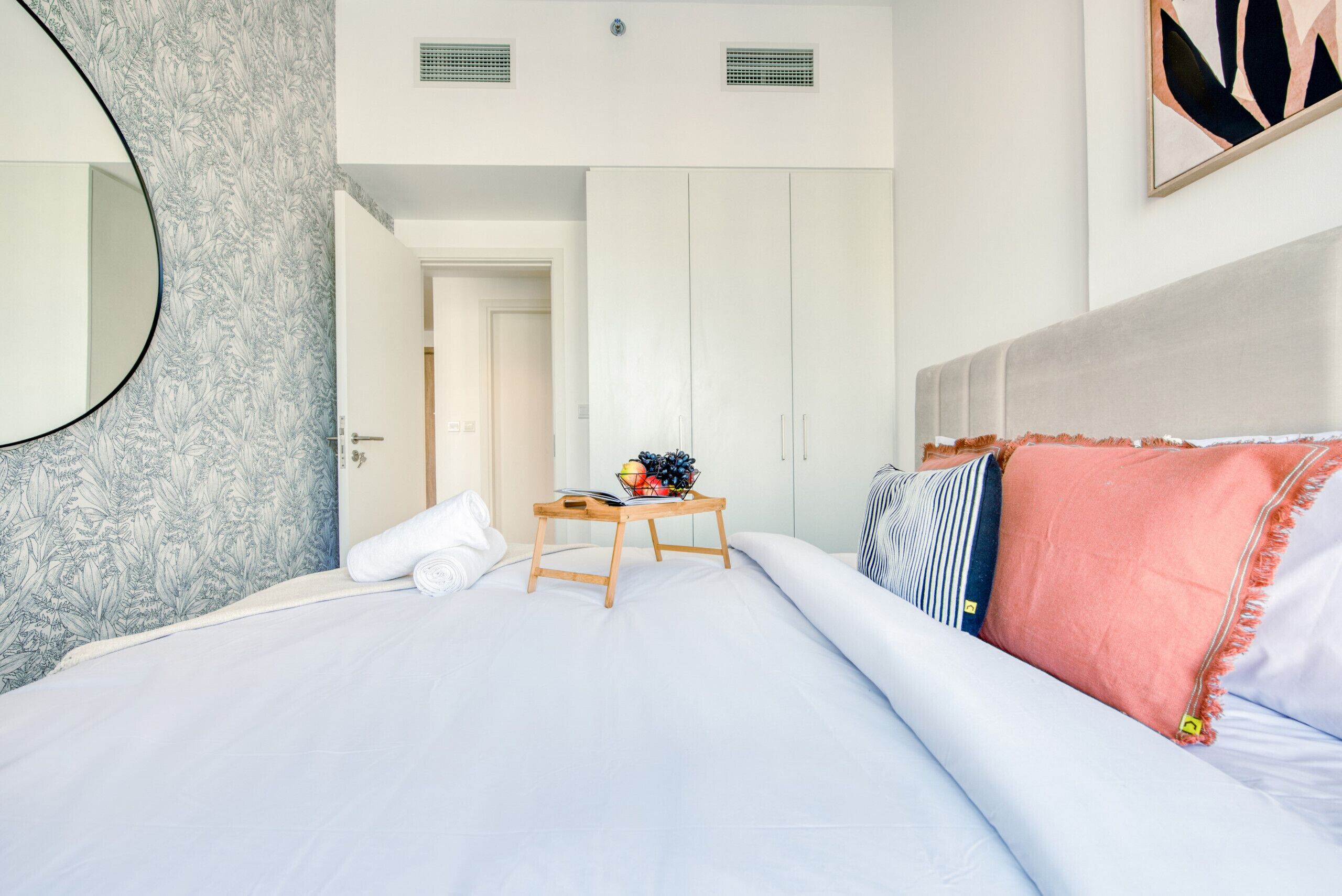 Un dormitorio con cama, una mesita de noche con frutero, un espejo y un armario.