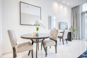 Quarto de hotel moderno com uma mesa de jantar redonda, duas poltronas estofadas, um vaso de planta e um espelho grande na parede.