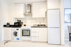 Uma cozinha compacta com armários brancos, forno embutido, micro-ondas, máquina de lavar e geladeira.