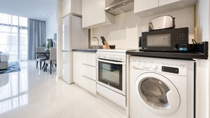 Uma cozinha moderna com armários brancos, uma coifa de aço inoxidável, micro-ondas, forno e máquina de lavar com abertura frontal.