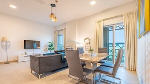 Ein modernes Wohnzimmer mit Sofa, Esstisch mit Stühlen, Fernseher und einem Balkon mit Vorhängen.