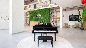 A grand piano in a spacious lobby with a green wall and a sign reading "UNA TOWN SQUARE DUBAI". - Spotless 1BR at UNA Town Square Dubailand by Deluxe Holiday Homes (Dubai)
