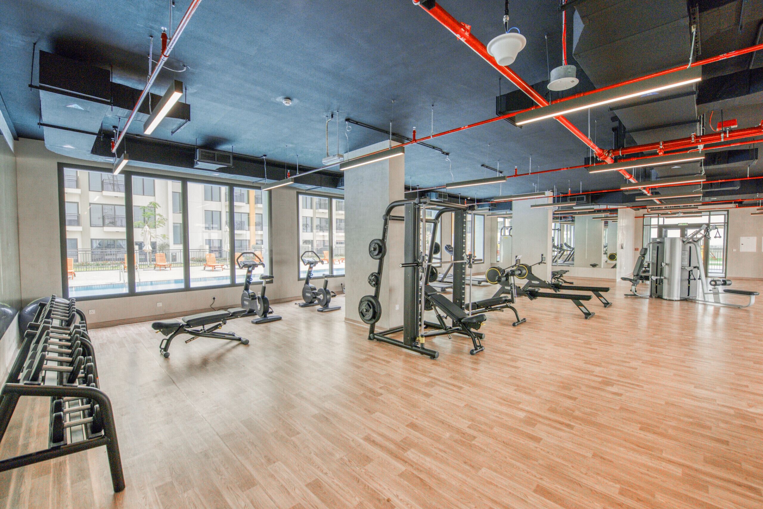 Una palestra con attrezzature per esercizi, ampie finestre e pavimento in legno.