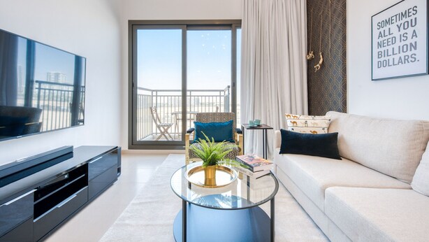 Ein modernes Wohnzimmer mit Flachbildfernseher, einem Glastisch mit Pflanze, einer Couch und einem großen Fenster mit Balkonblick.