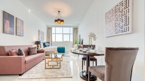 A modern living room with a sofa, coffee table, and a dining area with a table and chairs. - Intimate Studio in Damac Ghalia Jumeirah Village Circle by Deluxe Holiday Homes (Dubai)
